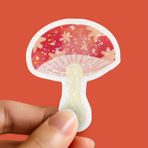 Hand holding a glittery mushroom-shaped sticker against a red background