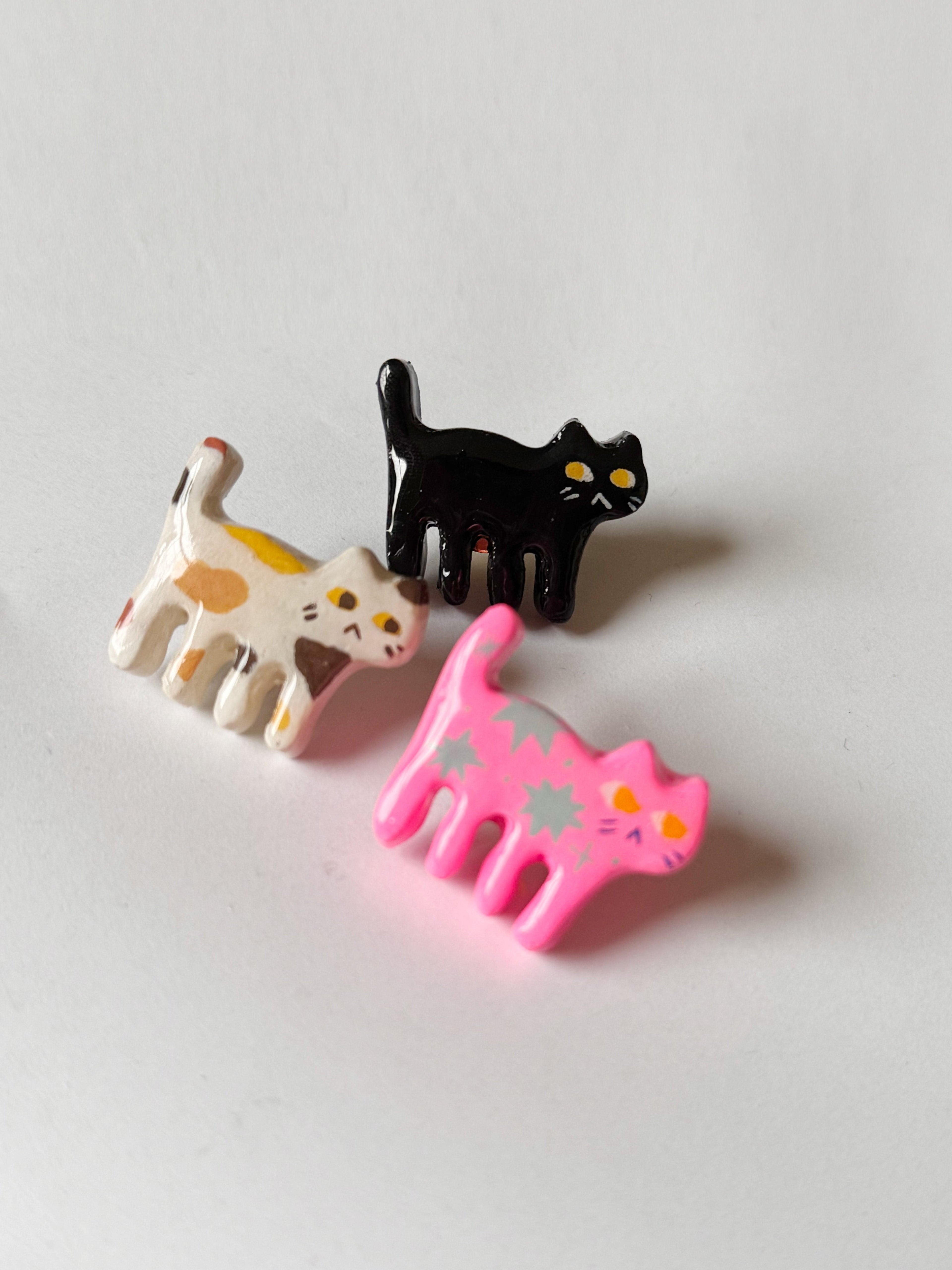 Three cat-shaped hair clips in black, pink, and multicolor on a white background