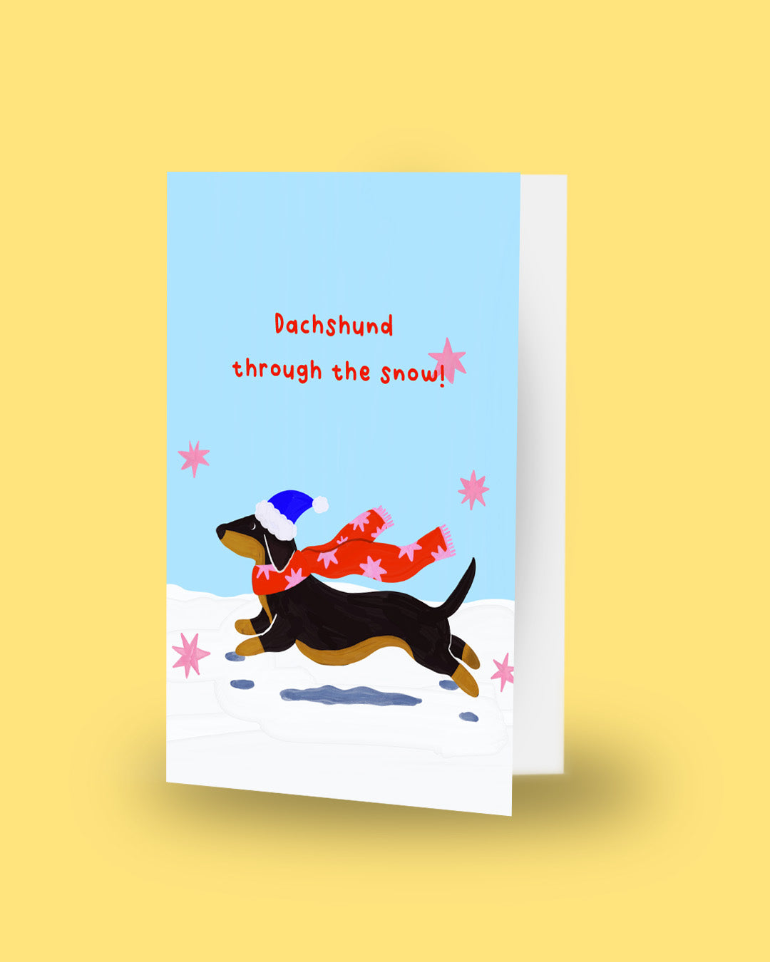 A Christmas-themed greeting card featuring a festive illustration with the text 'Pop the Buzz, Merry Christmas!' on a dark navy blue background with white stars, alongside a champagne bottle, a pink cocktail in a glass, and patterned spheres on a yellow surface.