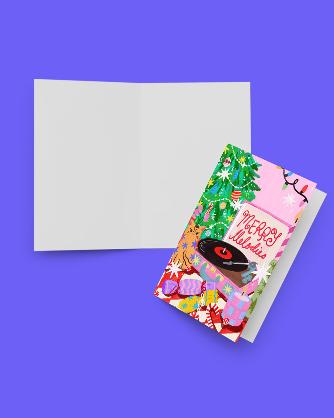 A Christmas greeting card set shown on a solid purple background, featuring an open blank white card and a closed card with a colorful festive illustration of a record player, tree, ornaments, and the words 'Merry Christmas'.