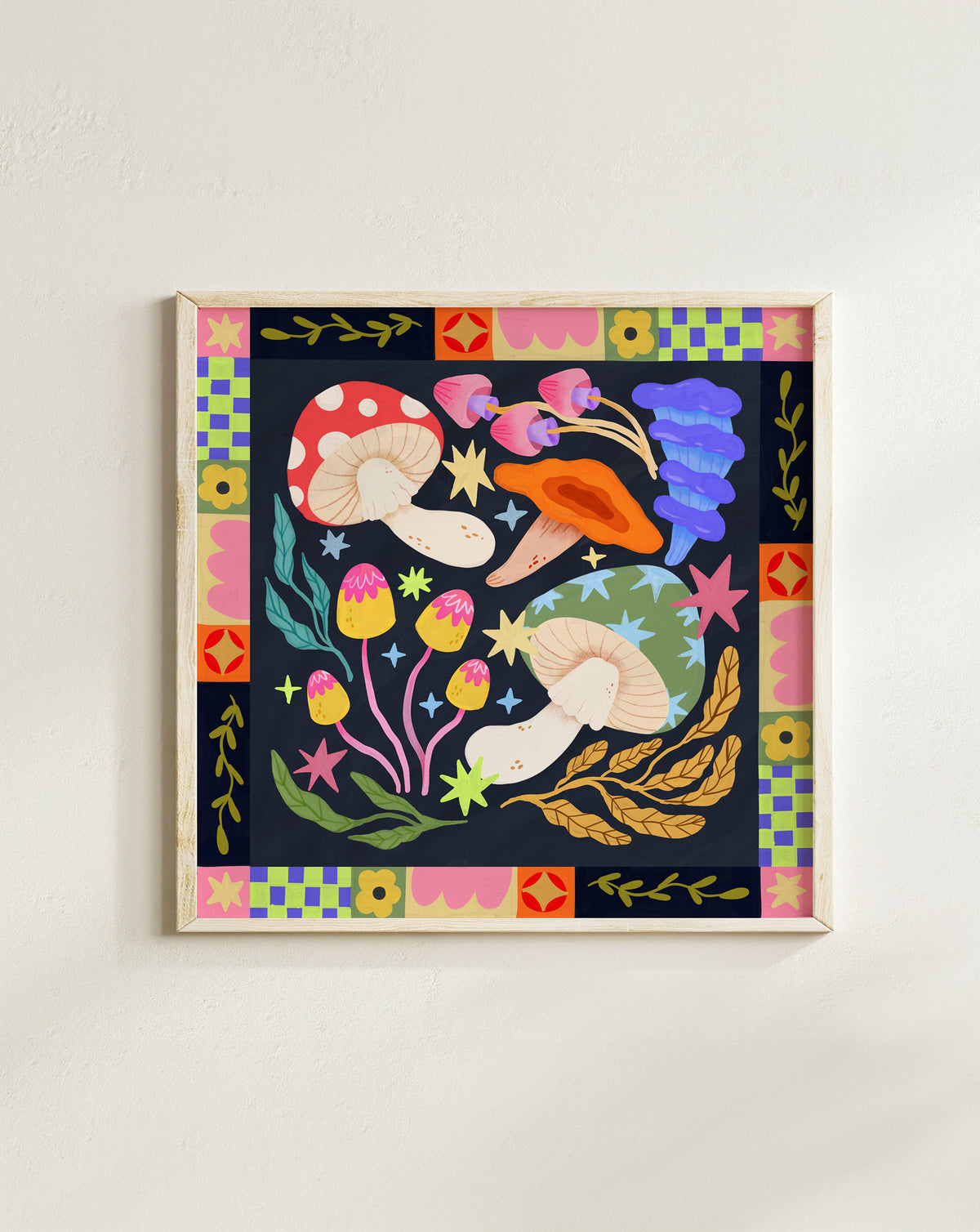 A framed square art print featuring a whimsical folk-art style illustration of mushrooms, flowers, stars, and leaves on a dark background, bordered by a colorful geometric pattern. The framed print is mounted on a plain off-white wall.