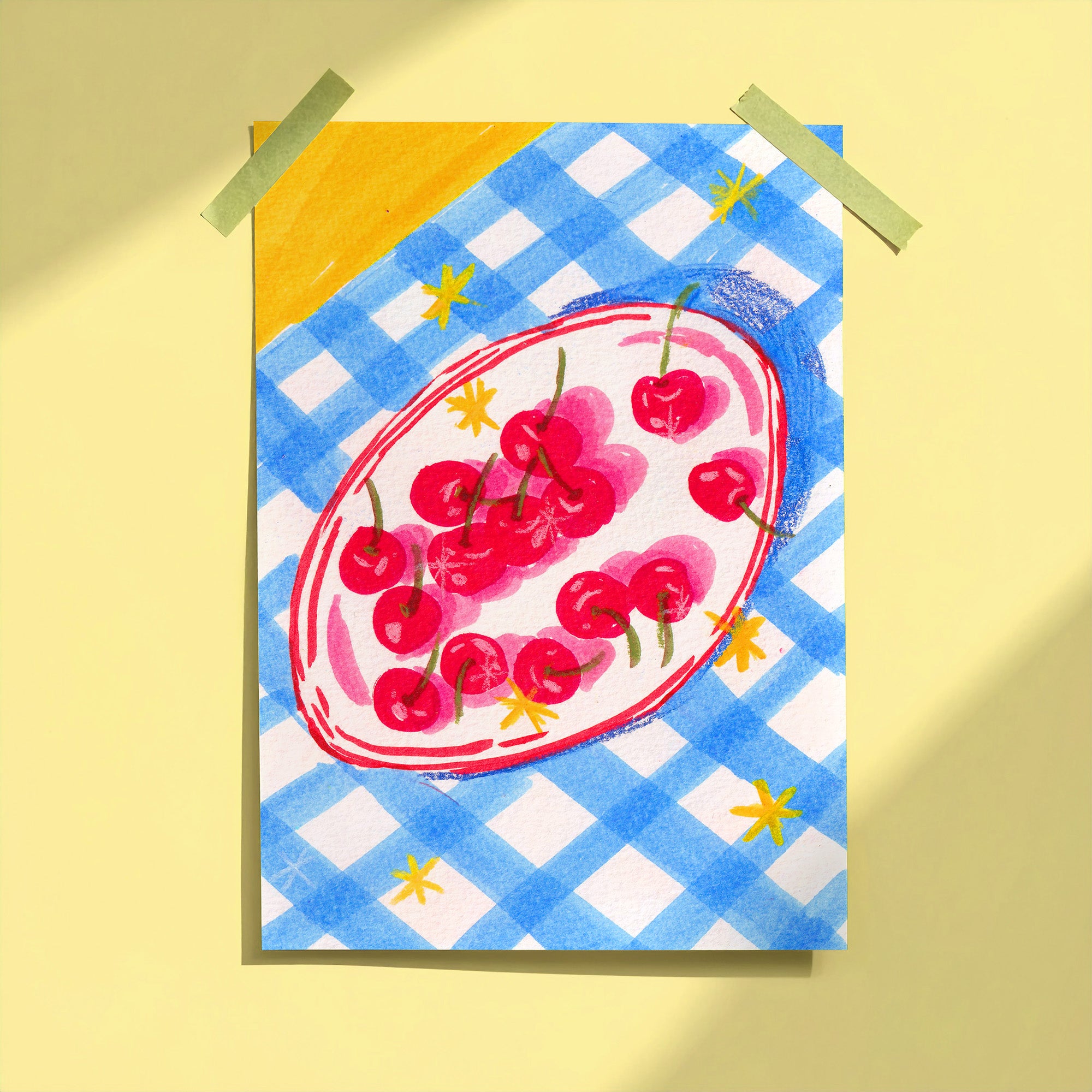 Bowl of Cherries art print taped to yellow wall showing red cherries on oval plate with blue gingham background, limited edition print by Ziyi Studio London
