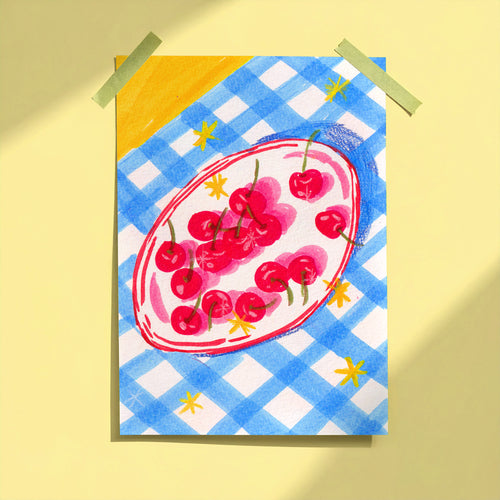 Bowl of Cherries art print taped to yellow wall showing red cherries on oval plate with blue gingham background, limited edition print by Ziyi Studio London