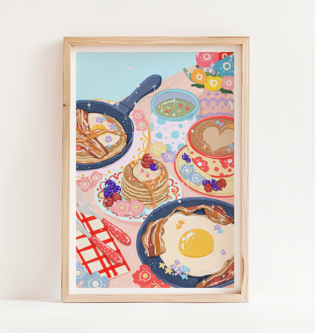 Framed artwork of a breakfast scene with pancakes, eggs, and coffee on a white wall.