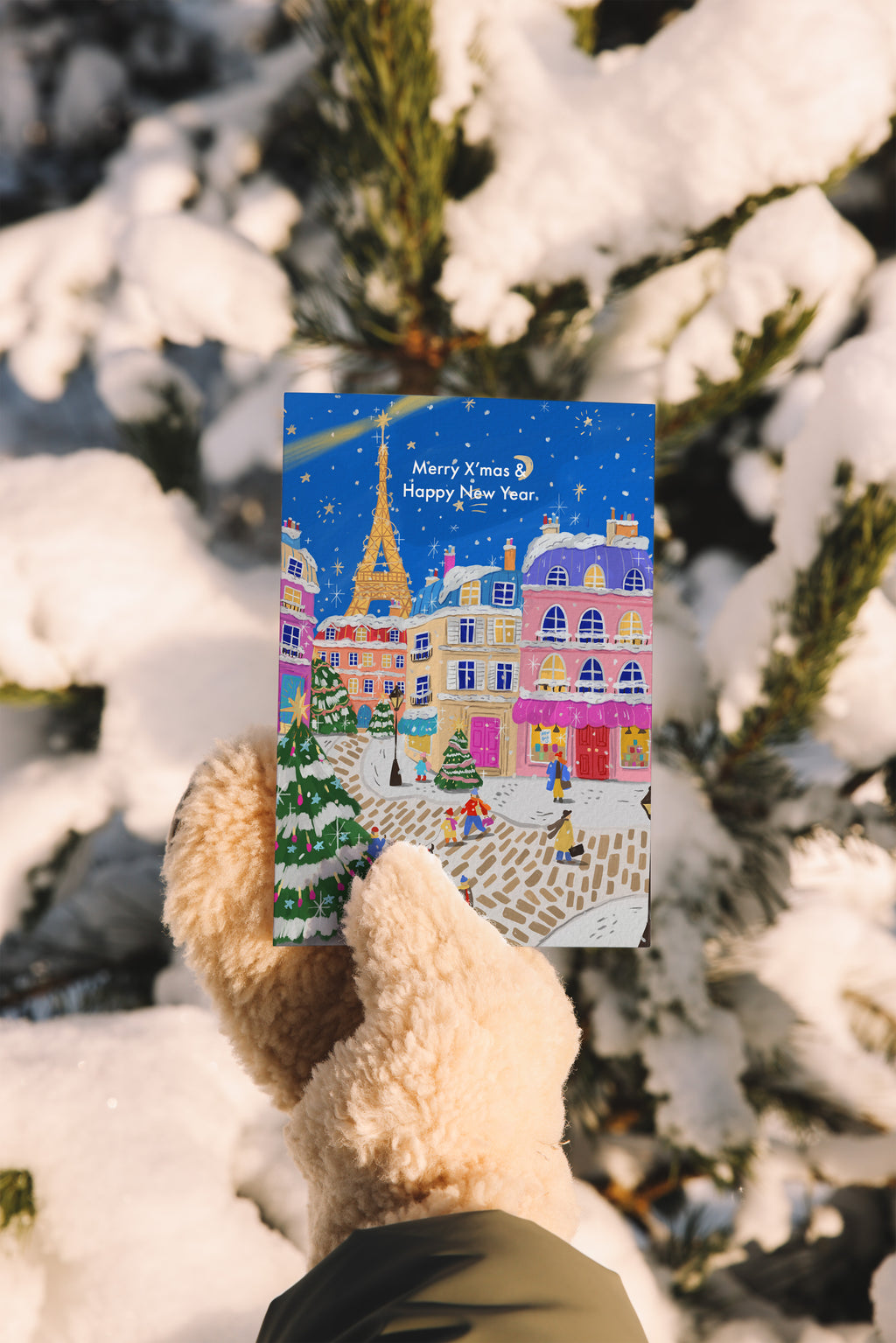 Person holding a Christmas card with a snowy village scene against a snowy background