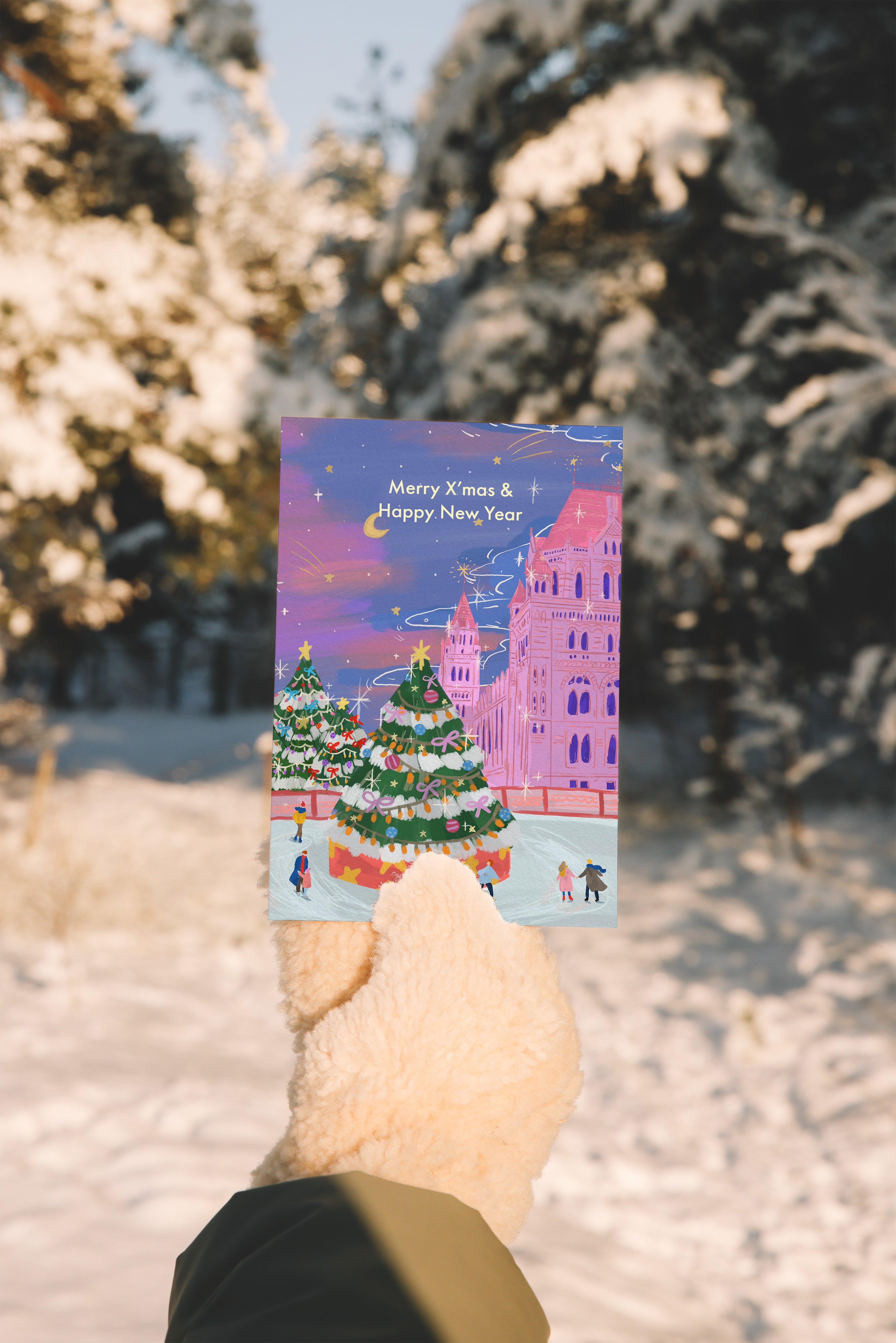 Hand holding a Christmas card with a snowy landscape and festive design.