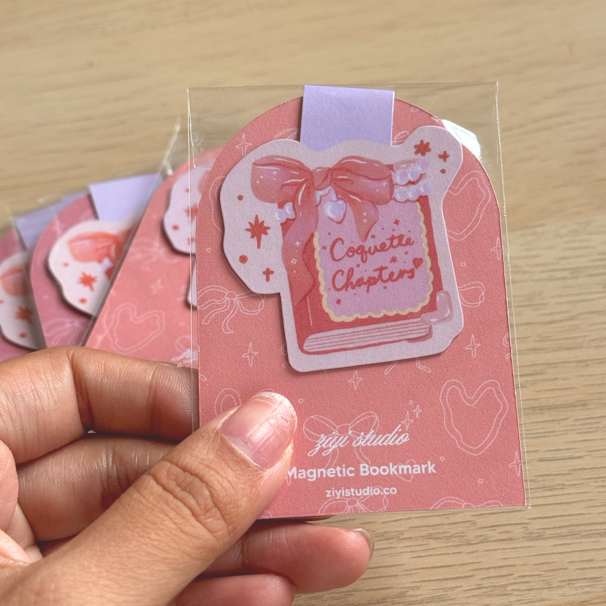 Pink magnetic bookmark with bow design held by a hand on a wooden surface