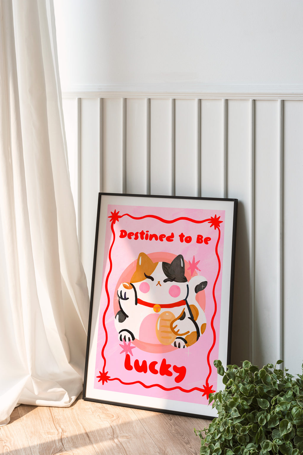 Framed artwork with a cat illustration and text 'Destined to be lucky' on a white wall.