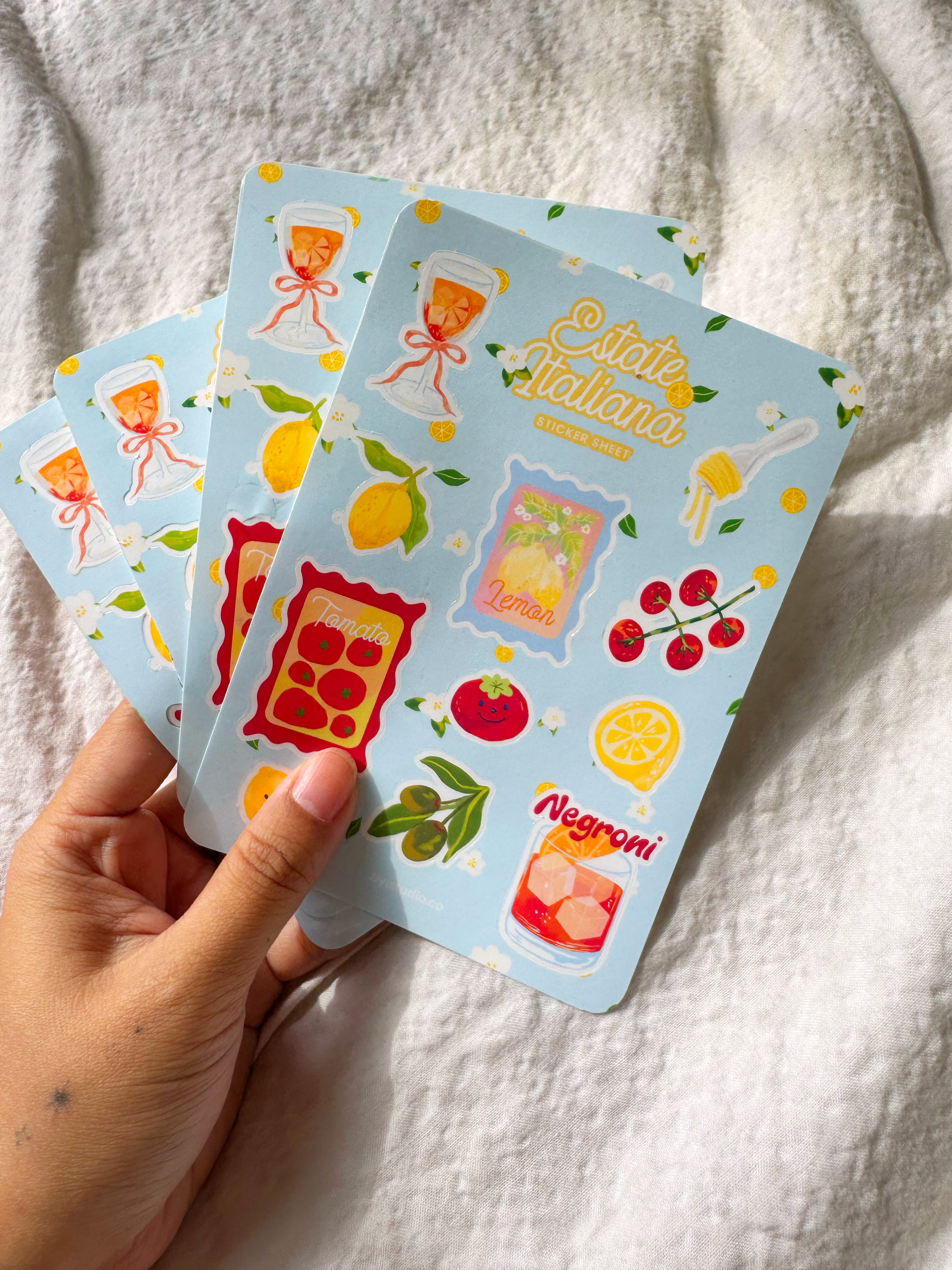 Italian summer-themed sticker sheet featuring hand-drawn illustrations of lemons, tomatoes, Aperol spritz, Negroni, pasta, and olives on a blue background.
