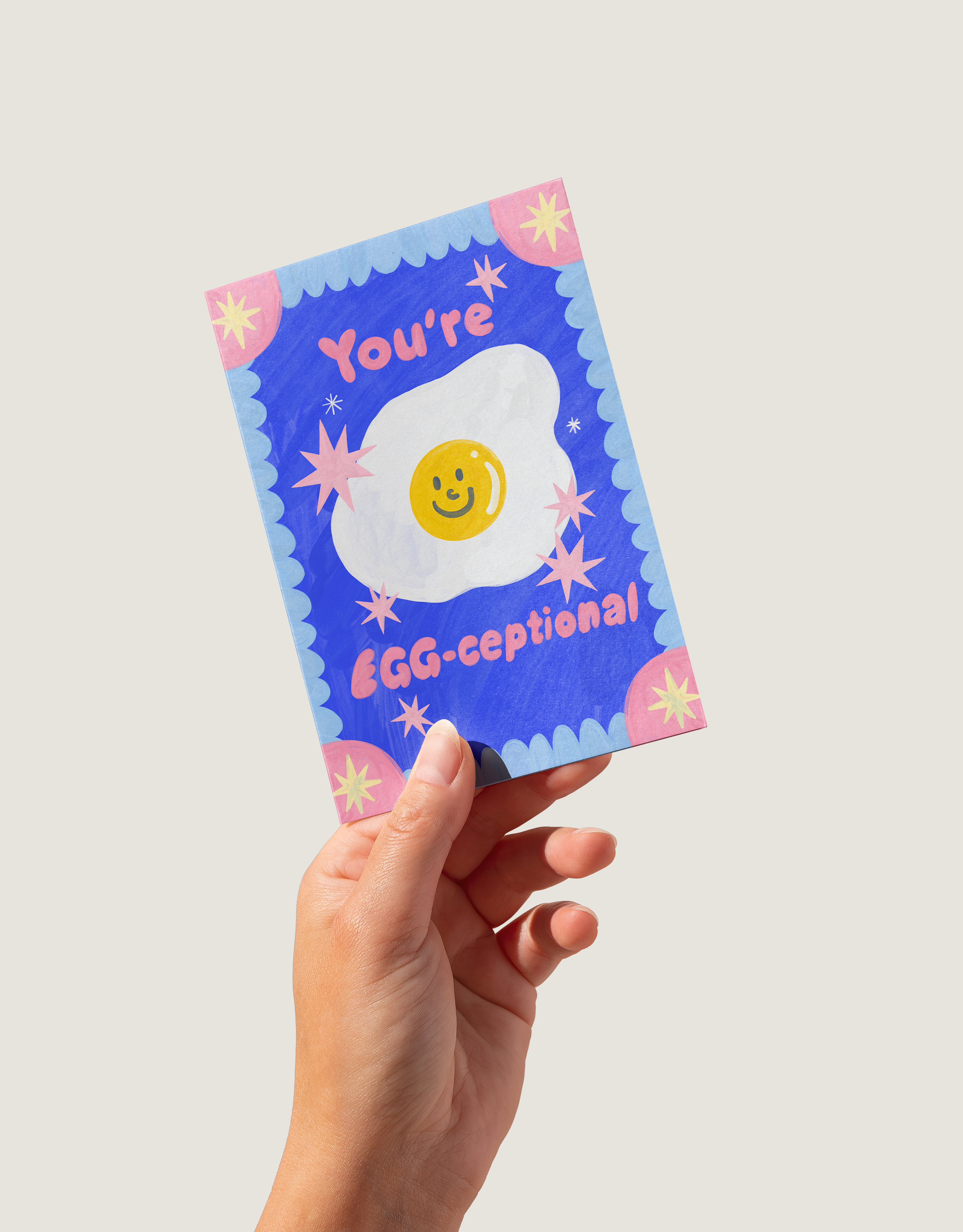 Hand holding a colorful card with an egg illustration and text on a light gray background