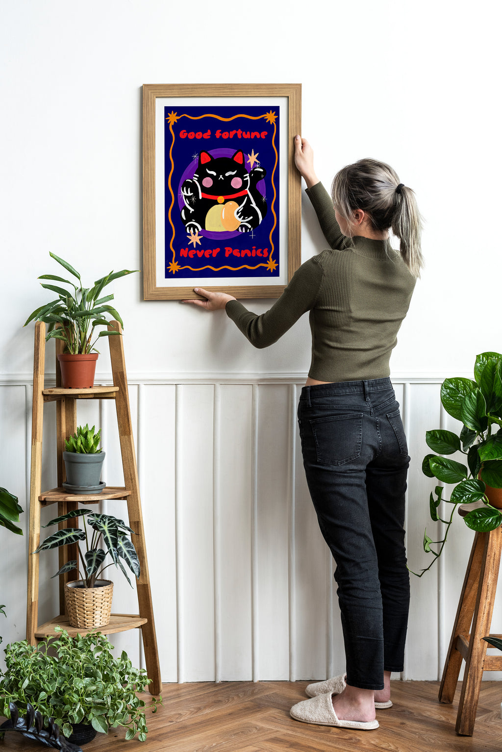 Person hanging a framed artwork of a cat with a bow tie on a wall.