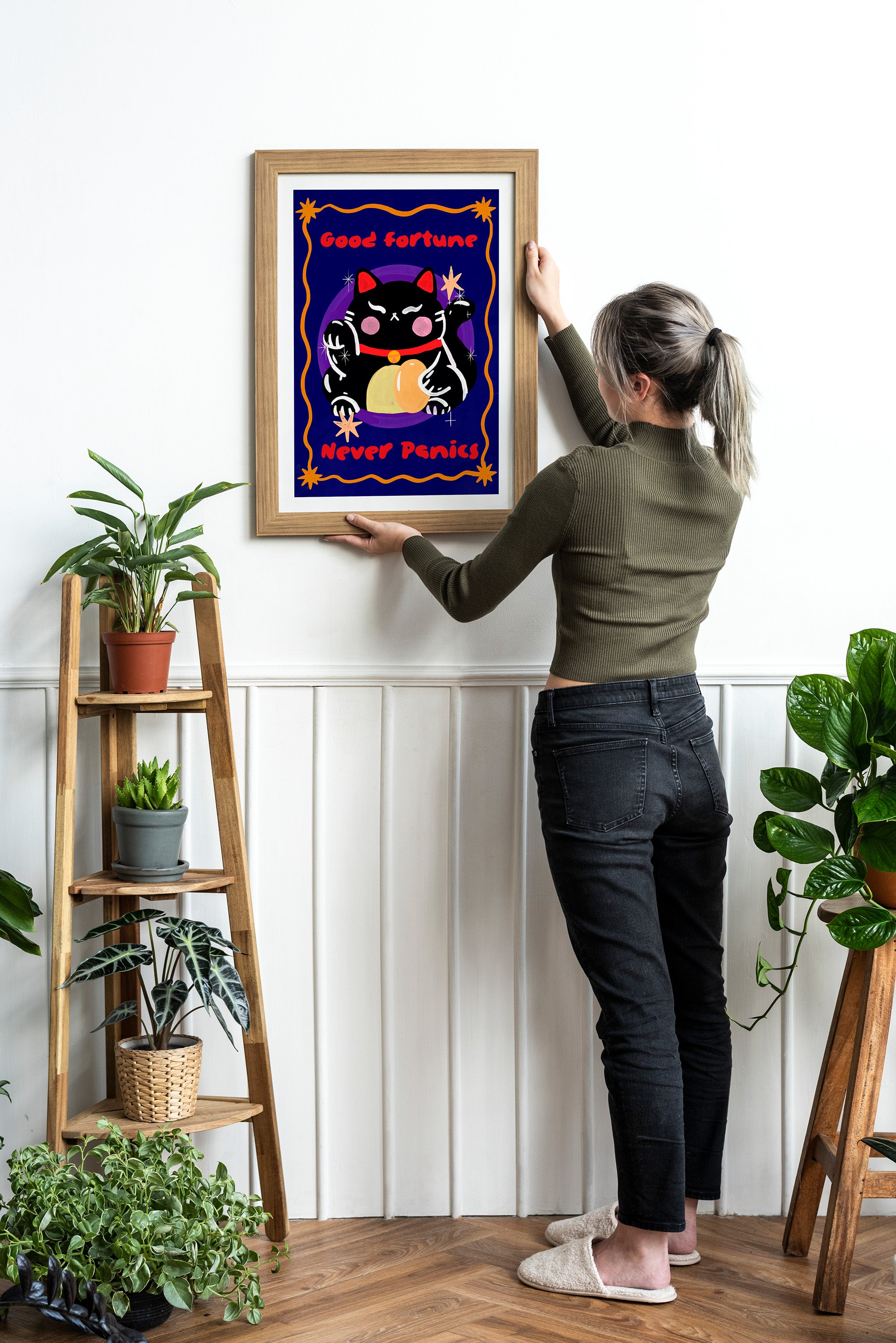 Person hanging a framed artwork of a cat with a bow tie on a wall.