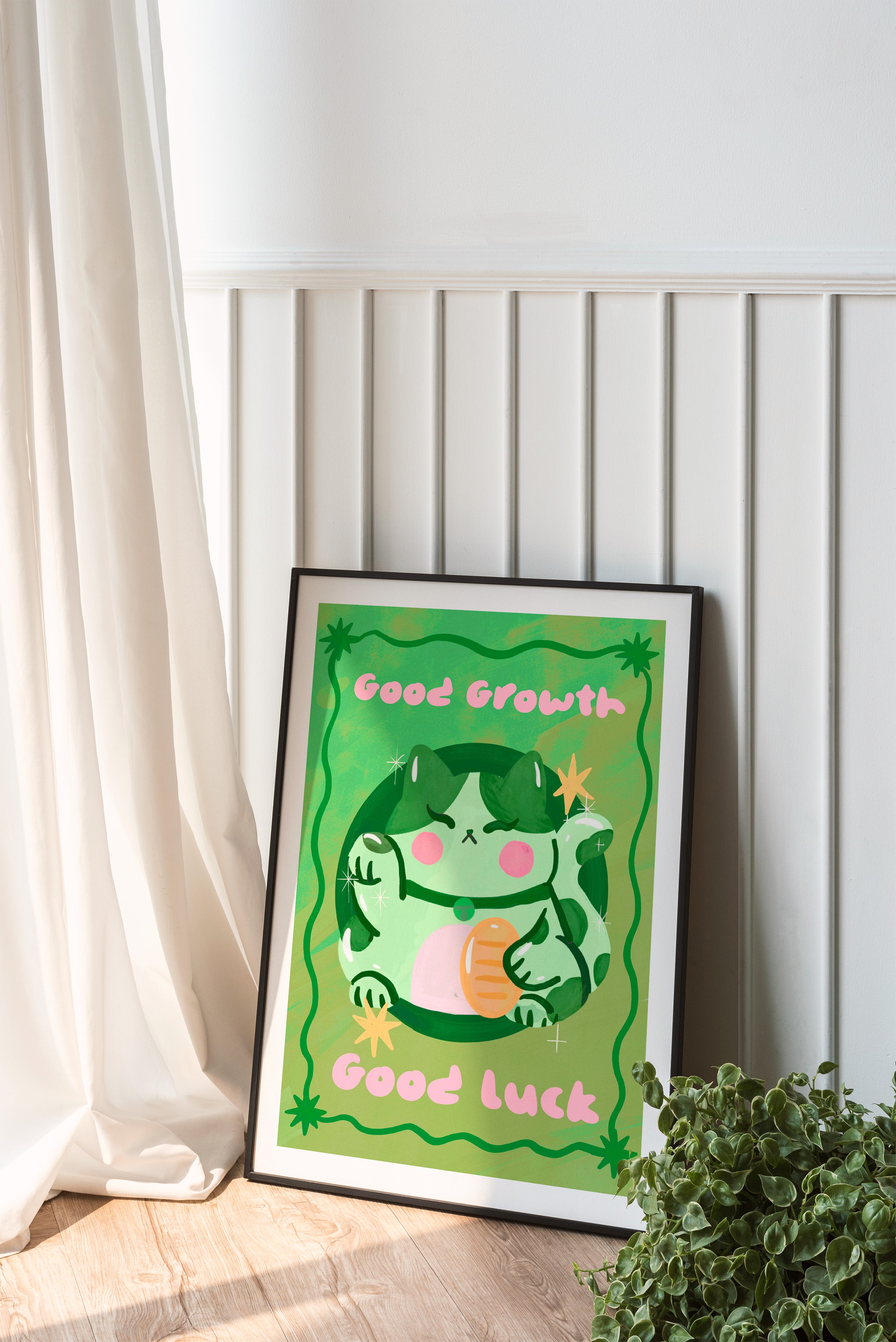 Framed artwork with a green character and text 'Good Growth, Good Luck' on a white wall.