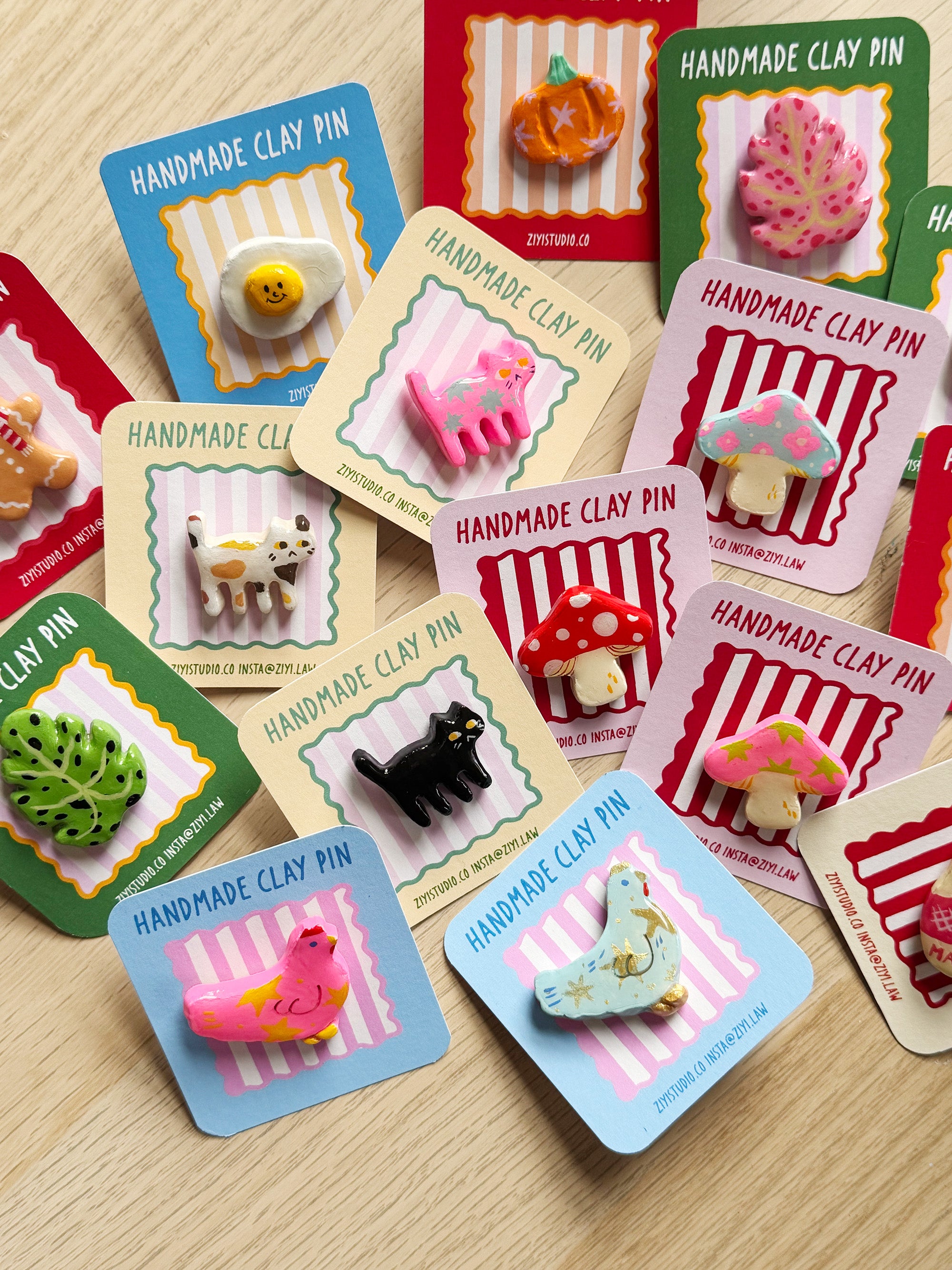 Collection of handmade clay pins on colorful cards displayed on a wooden surface.