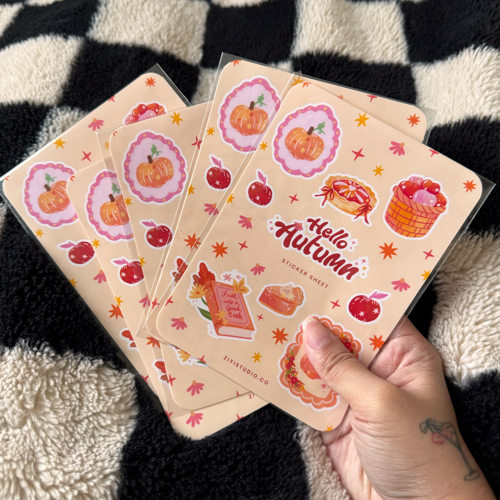 Hand holding a 'Hello Autumn' sticker sheet with fall-themed designs on a checkered background.