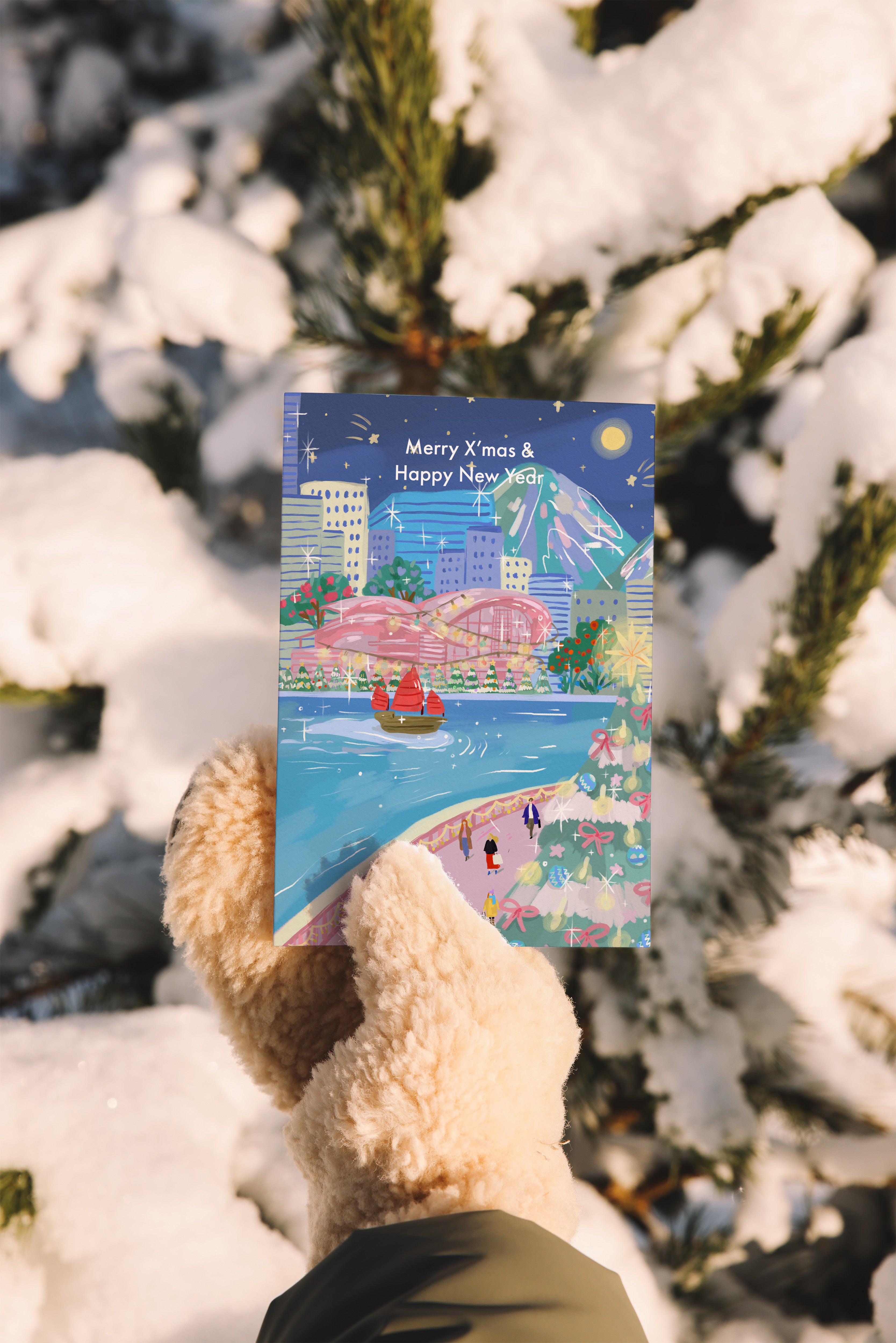 Person holding a Christmas card with a festive design against a snowy background