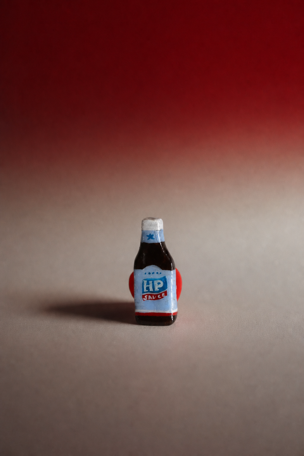 A miniature bottle of HP Sauce, styled like a real sauce bottle with a white cap, blue and red label, and dark brown contents, standing on a beige surface against a red-to-beige gradient background.