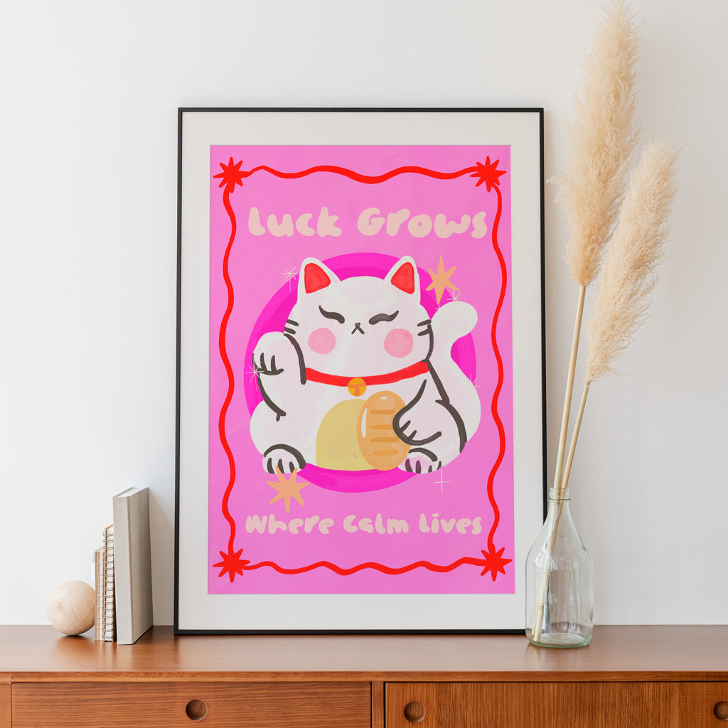 Framed artwork with a cartoon cat and pink background on a wooden surface.