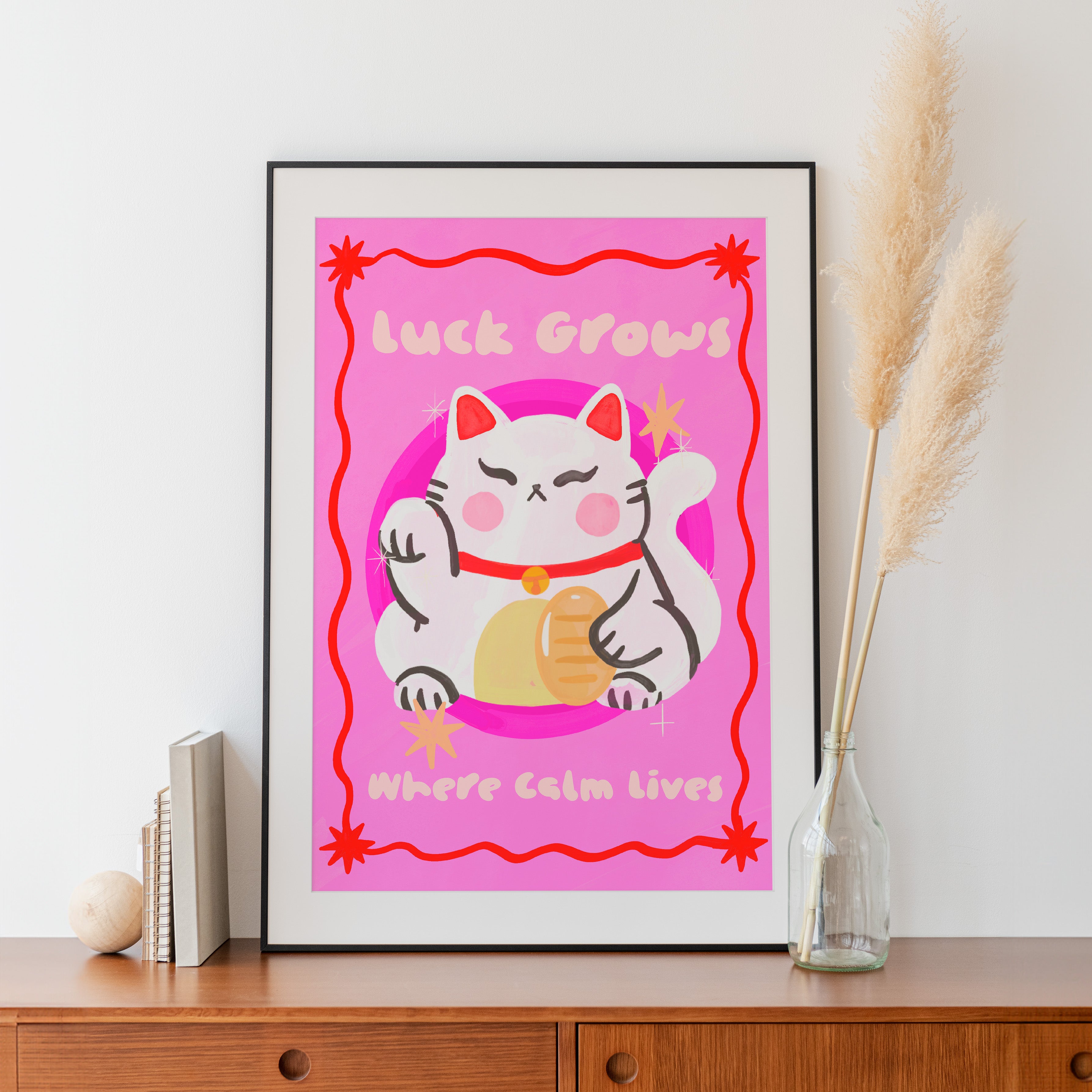 Framed artwork with a cartoon cat and pink background on a wooden surface.