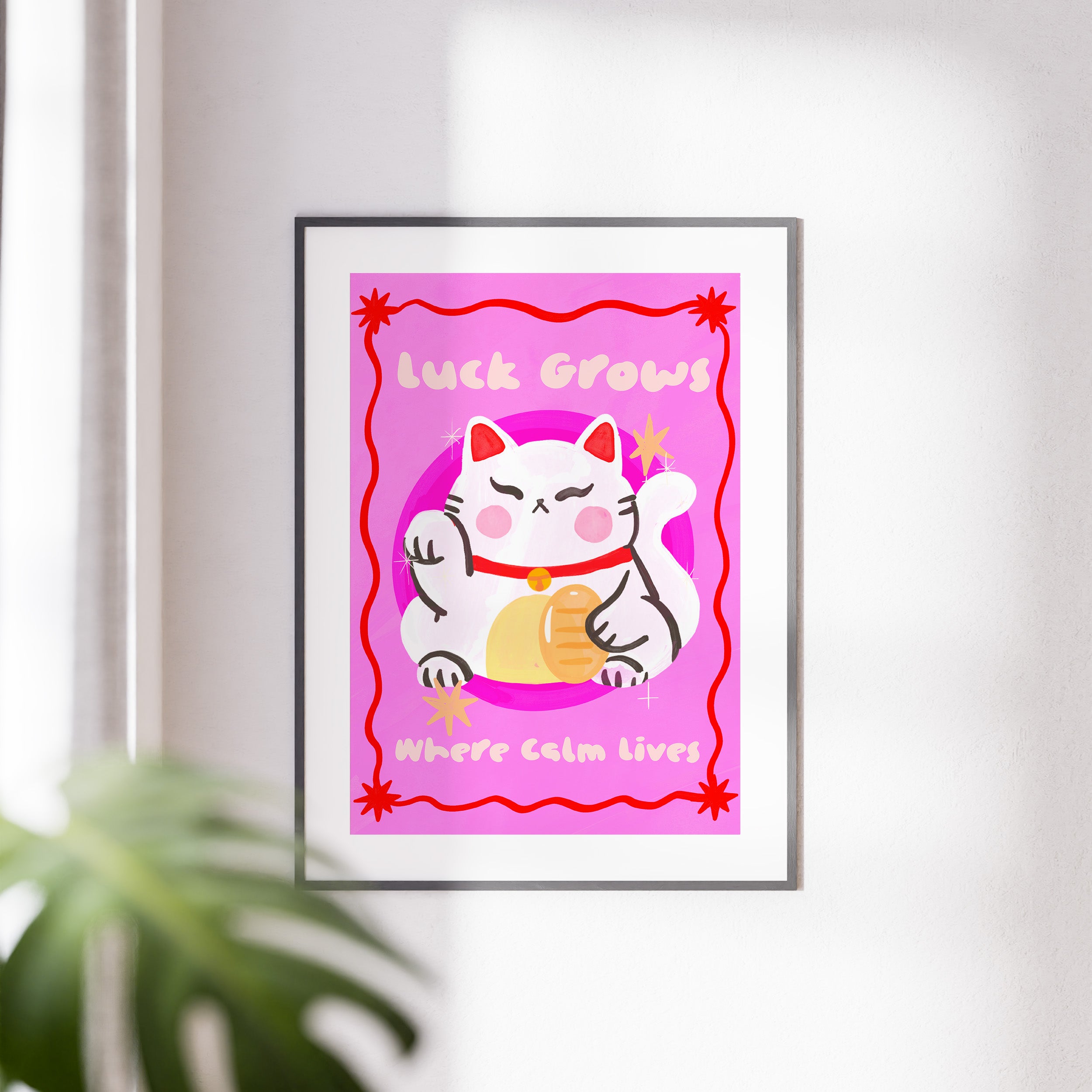 Framed artwork with a cartoon cat and text on a pink background, placed on a white wall.