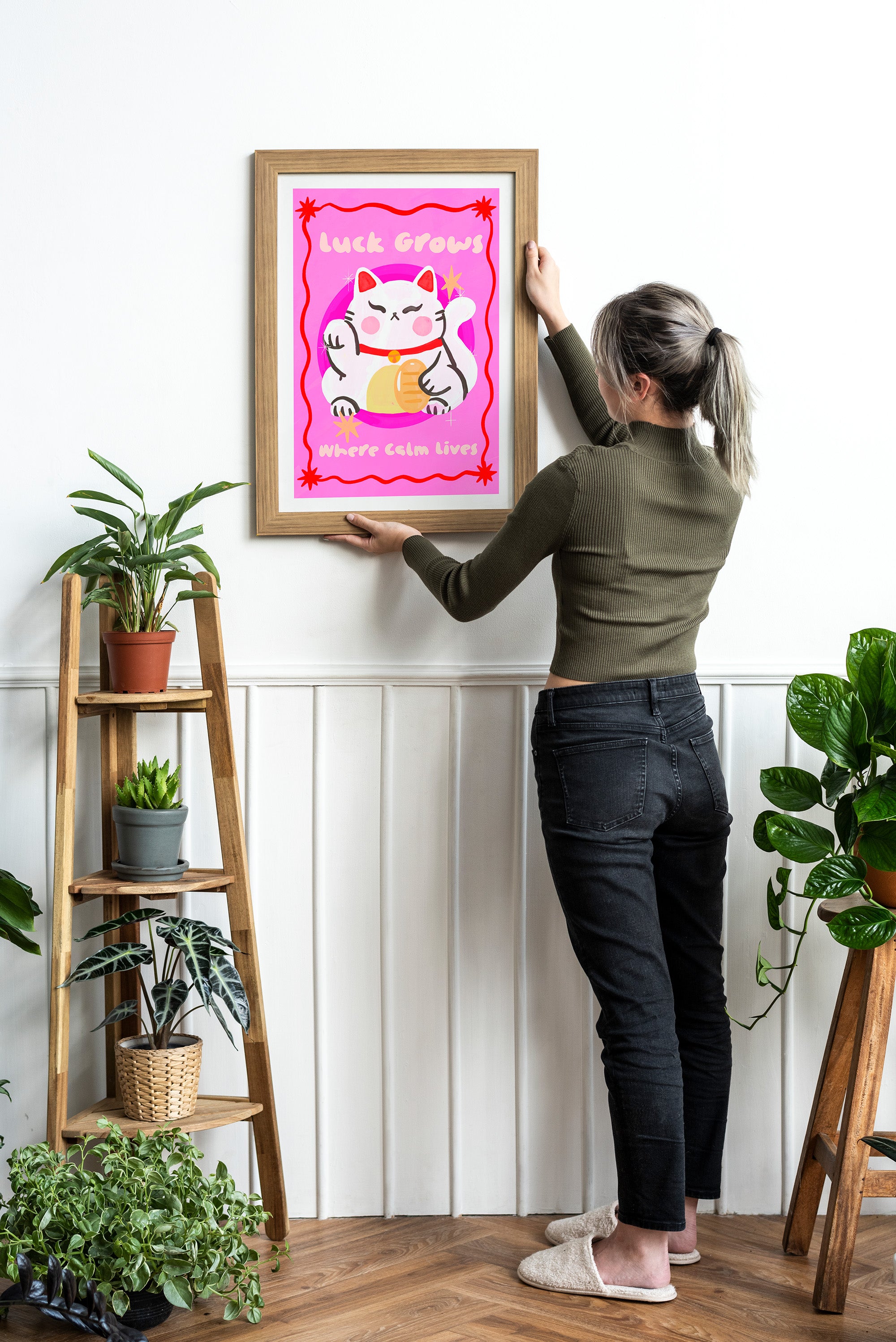 Person hanging a framed artwork of a cartoon cat on a wall