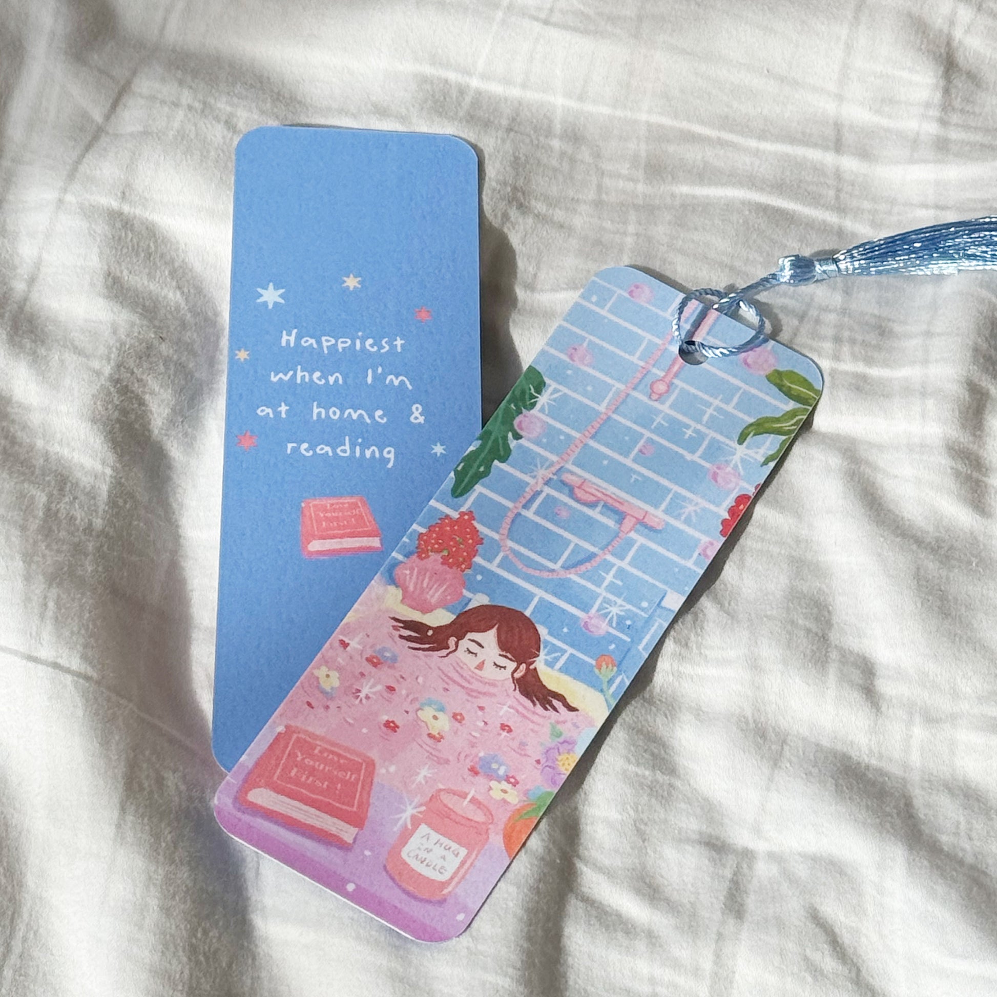 Handmade double-sided bookmark titled “Manifest & Relax,” featuring a cozy self-care illustration on the front and the quote “Happiest when I’m at home & reading” on the back. Matte finish with optional tassel.