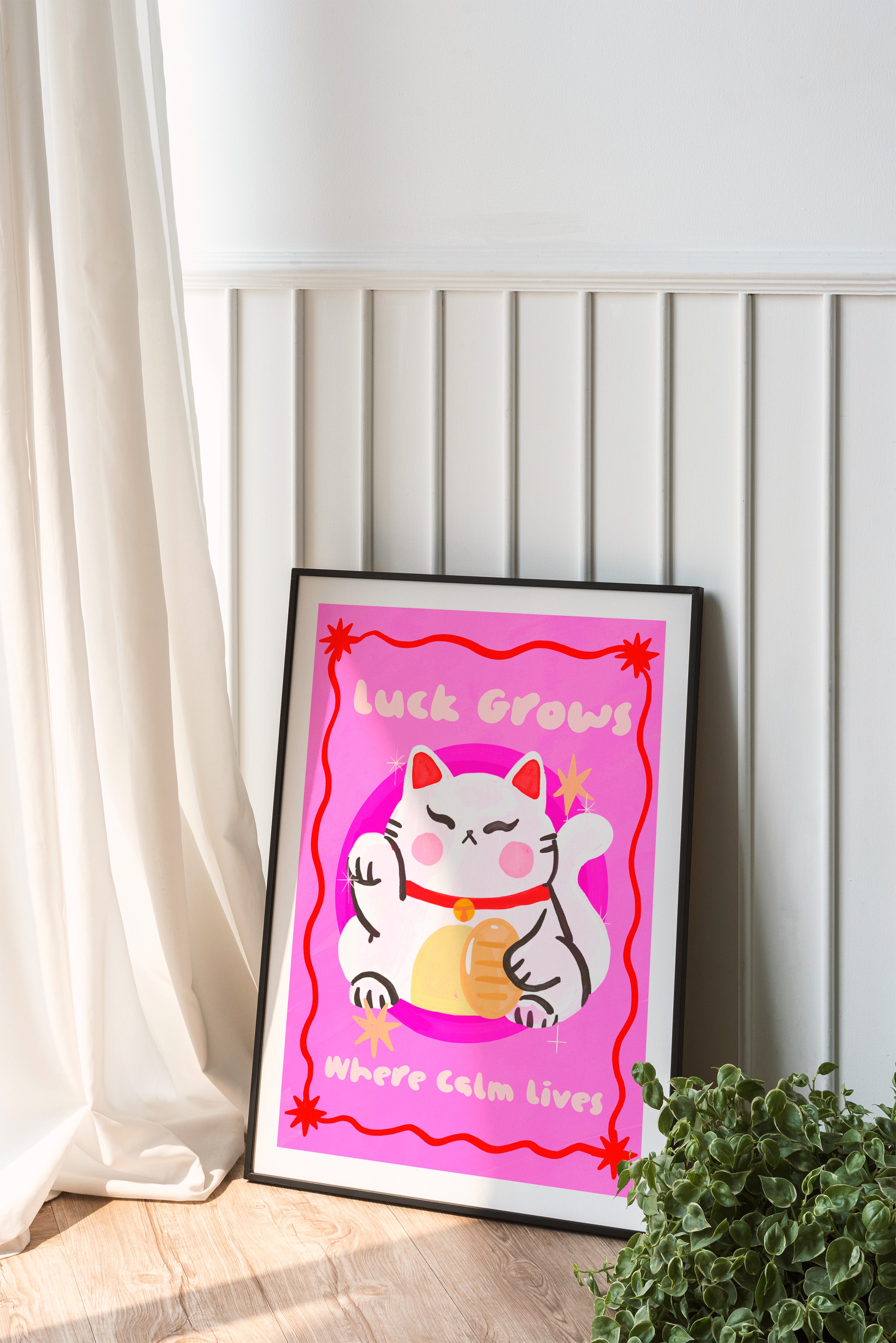 Framed artwork with a cartoon cat on a pink background, leaning against a white wall.
