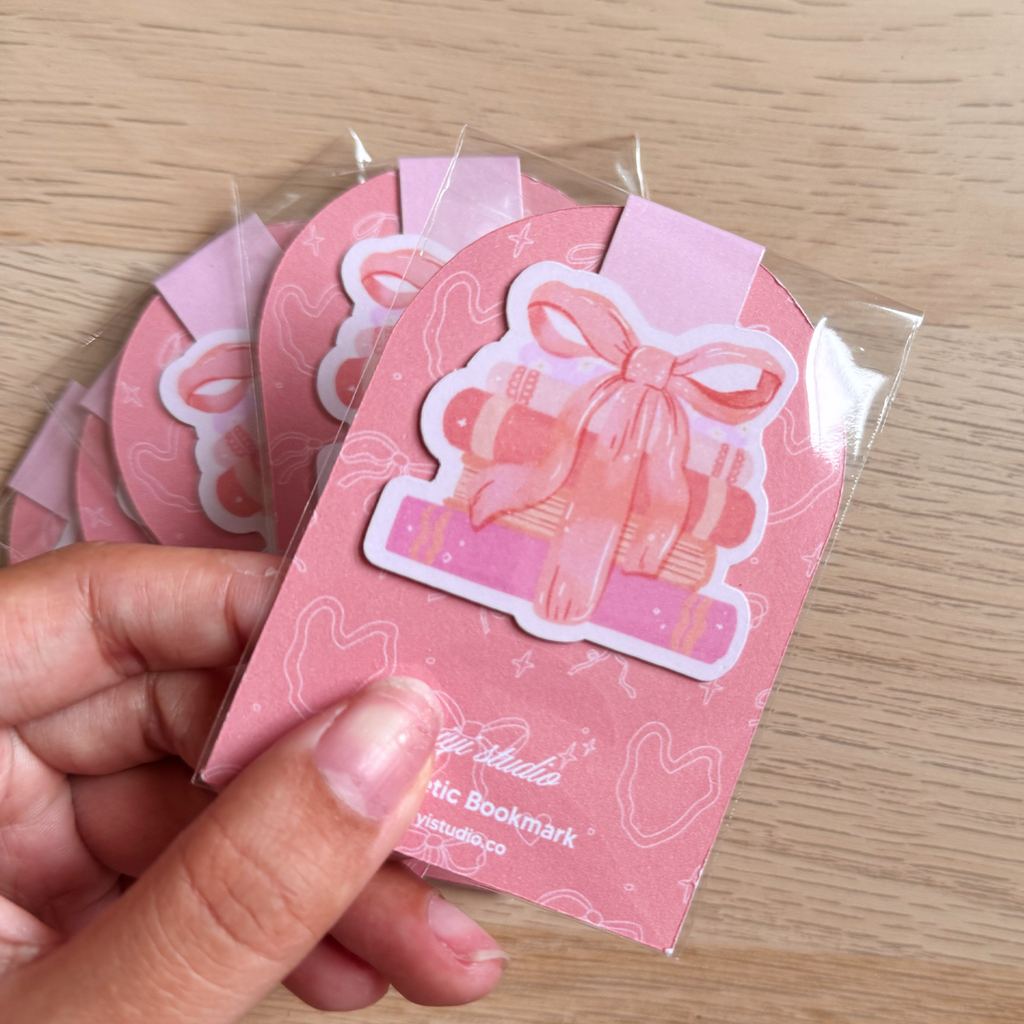 Pink bookmark with bow design held by a hand on a wooden surface