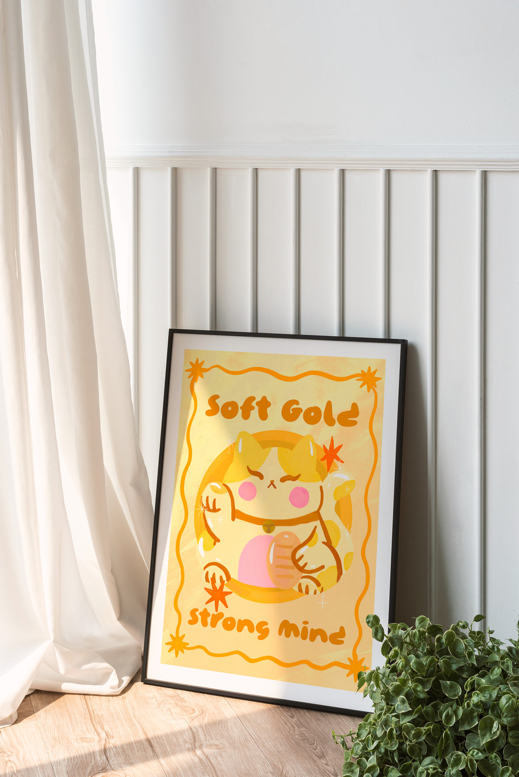 Framed artwork with a cartoon character and text 'Soft Gold Strong Mind' on a white wall.