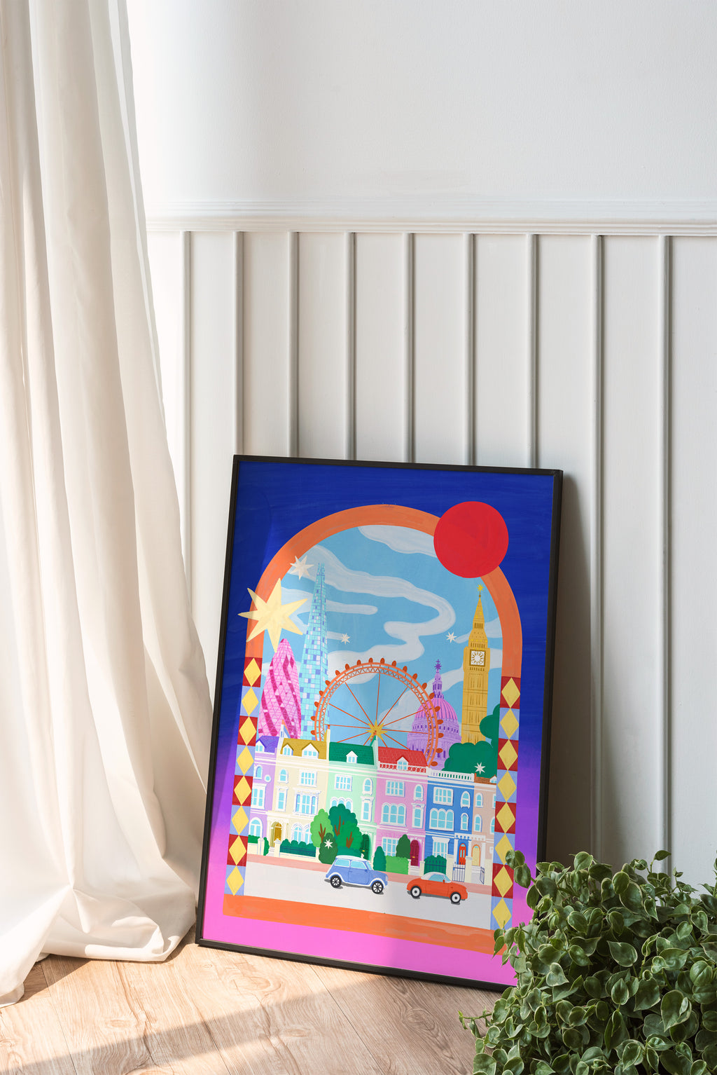 Colorful framed artwork of a cityscape with a red sun on a white wall.