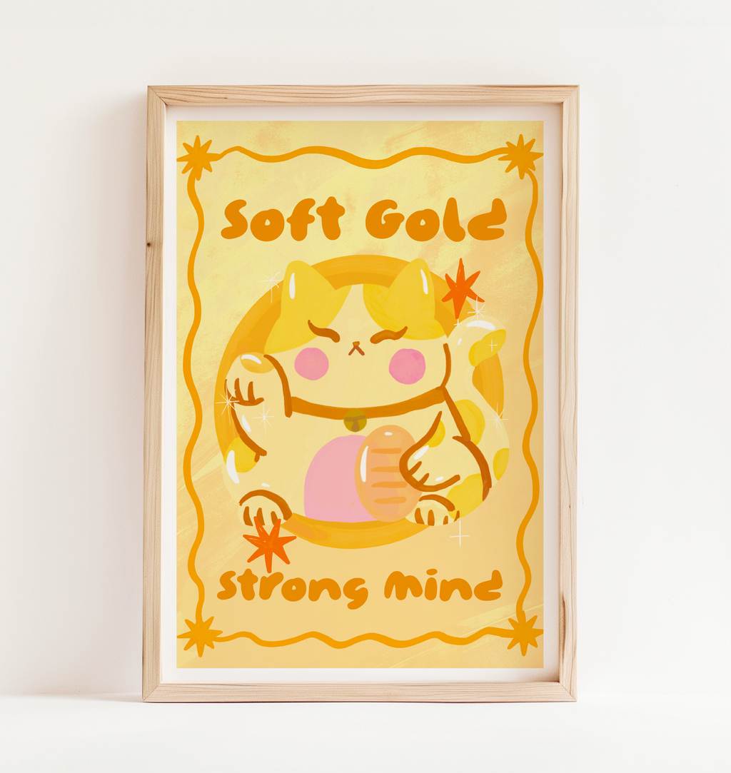 Framed artwork with a cartoon cat character and text 'Soft Gold Strong Mind' on a yellow background.