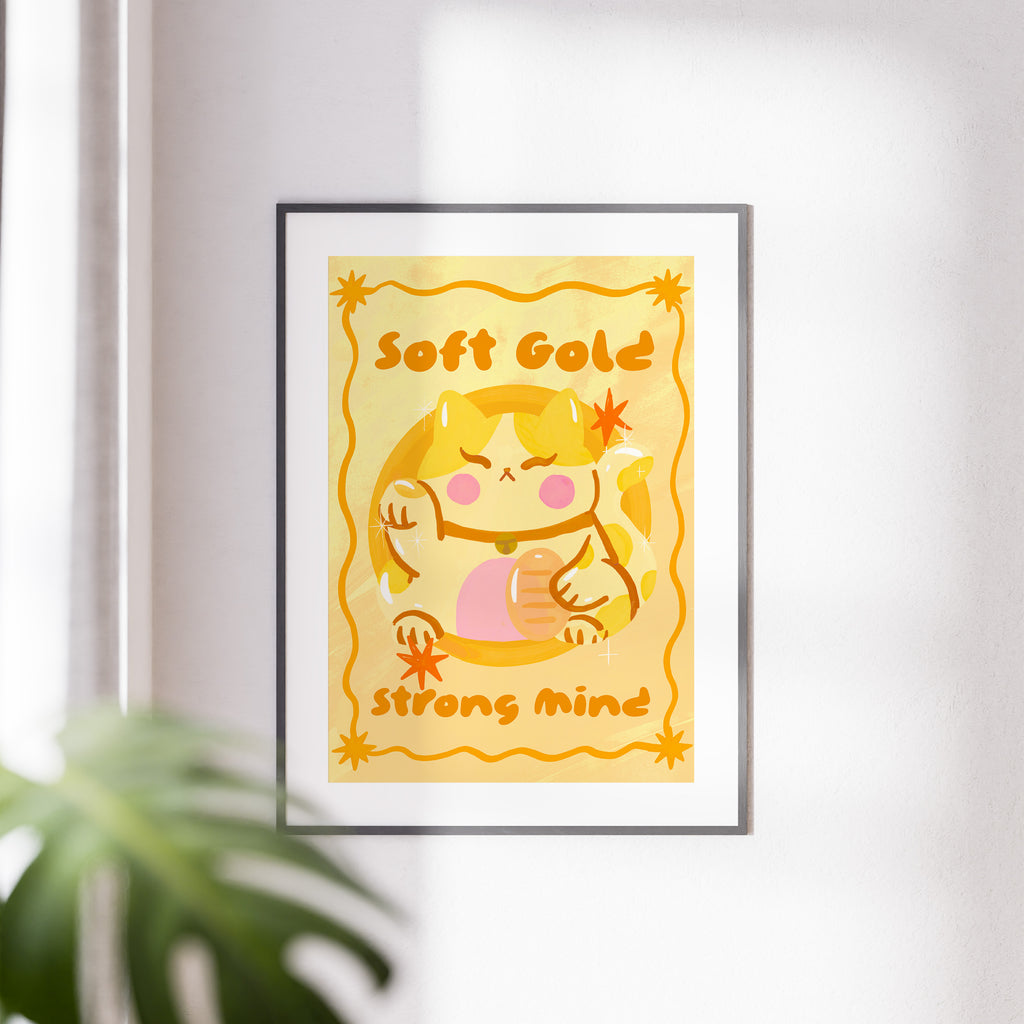 Framed artwork with a cartoon character and text 'Soft Gold Strong Mind' on a yellow background.